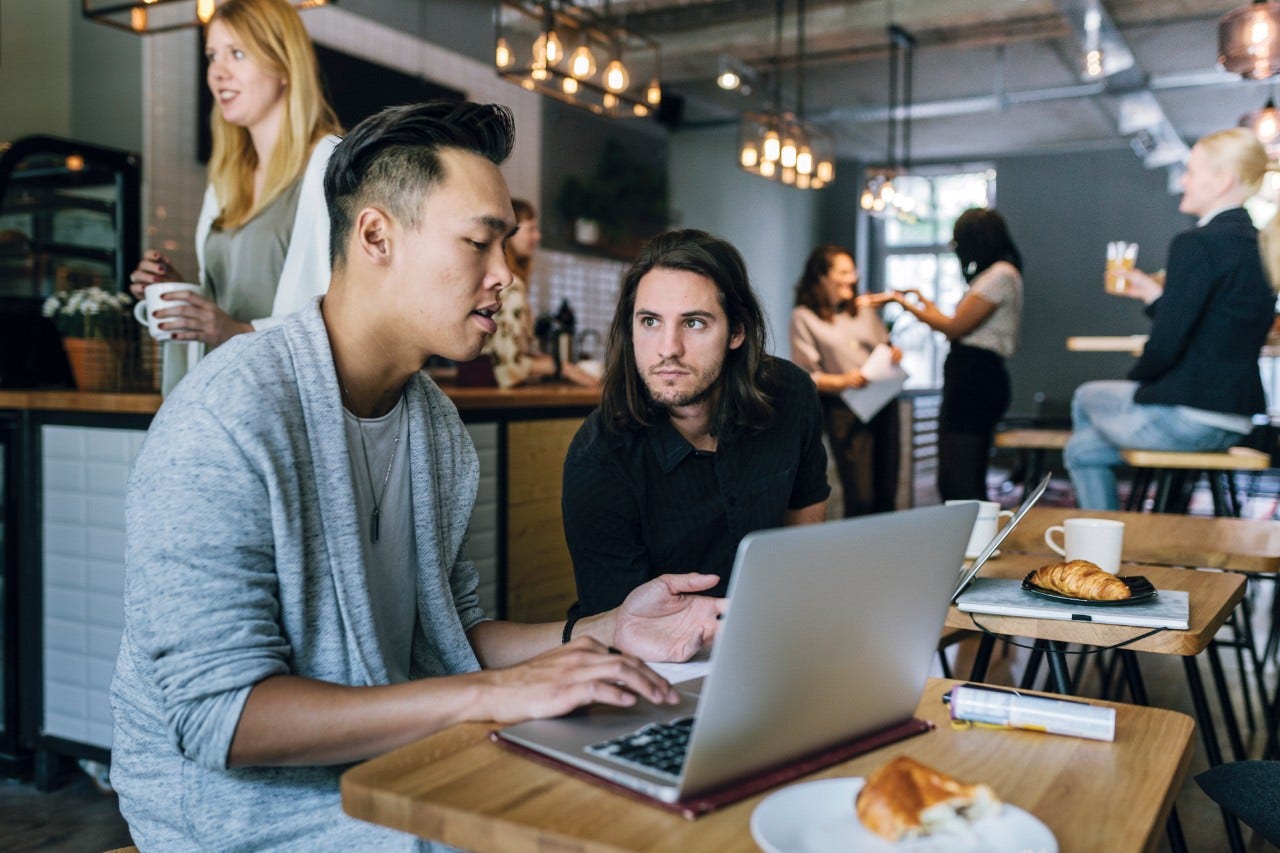 Two young entrepreneurs sitting in a busy business cafe, working and discussing projects and ideas.